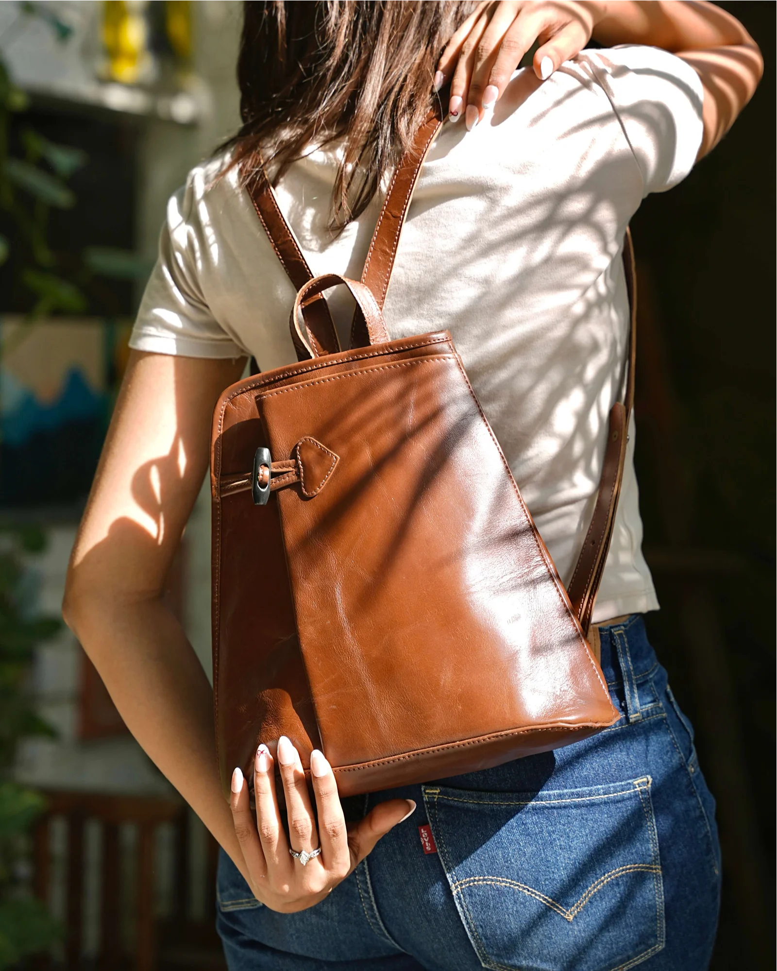 Person wearing a brown real leather backpack with a blurred background. 100% genuine full grain leather, natural patina