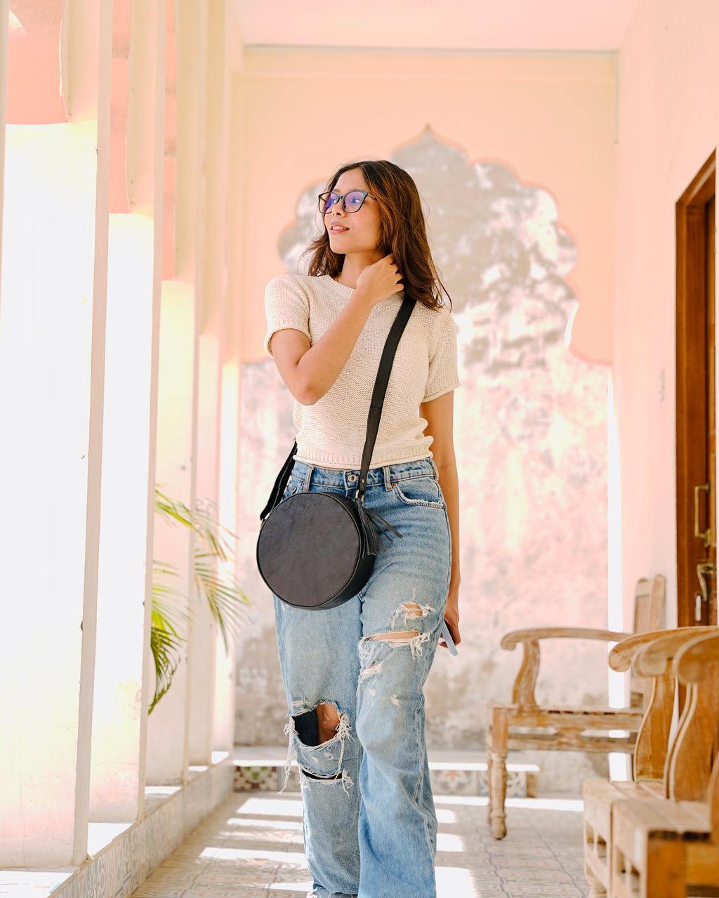 woman holding a black sling crossbody circular aesthetic leather bag