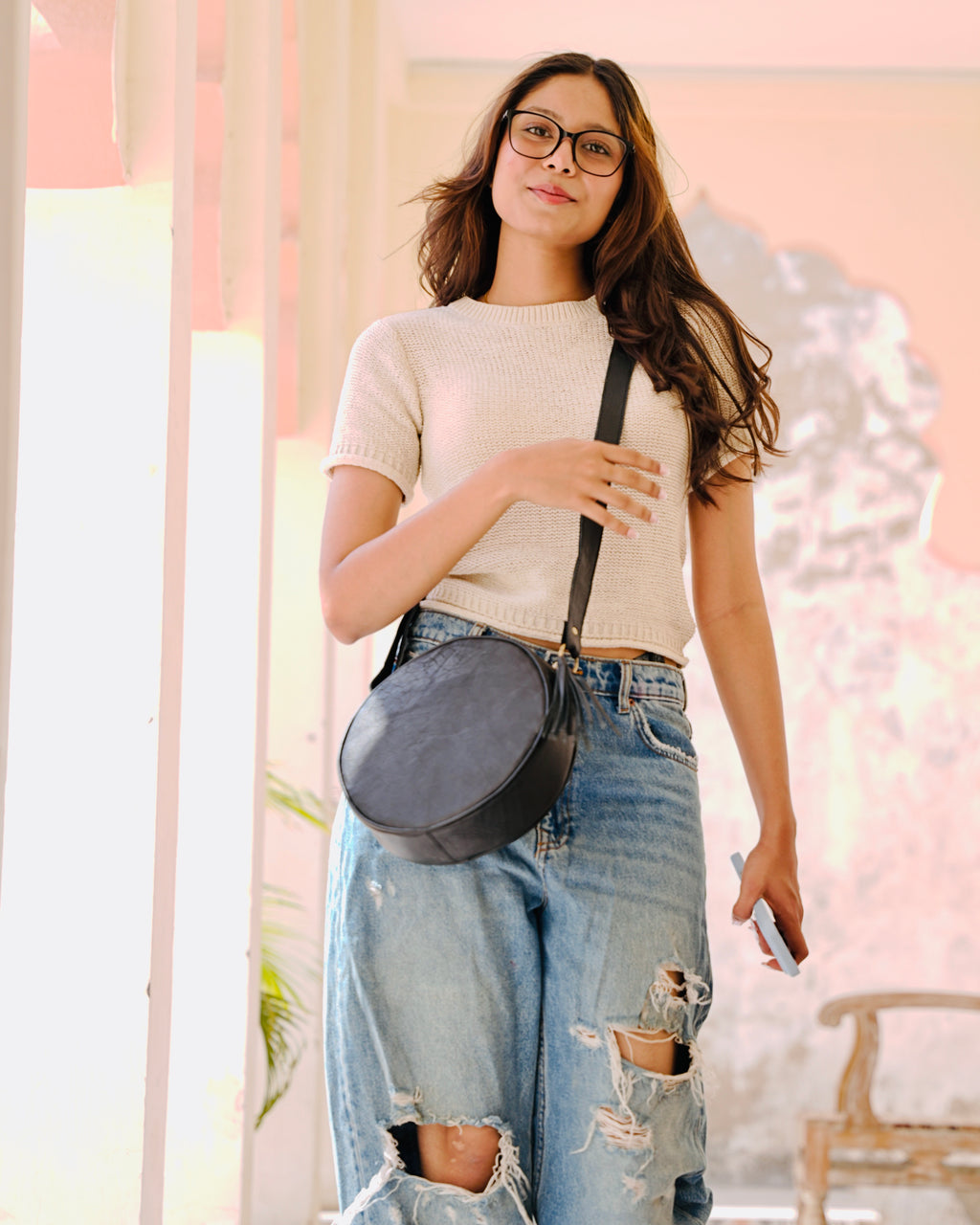 woman holding a black sling crossbody circular aesthetic leather bag