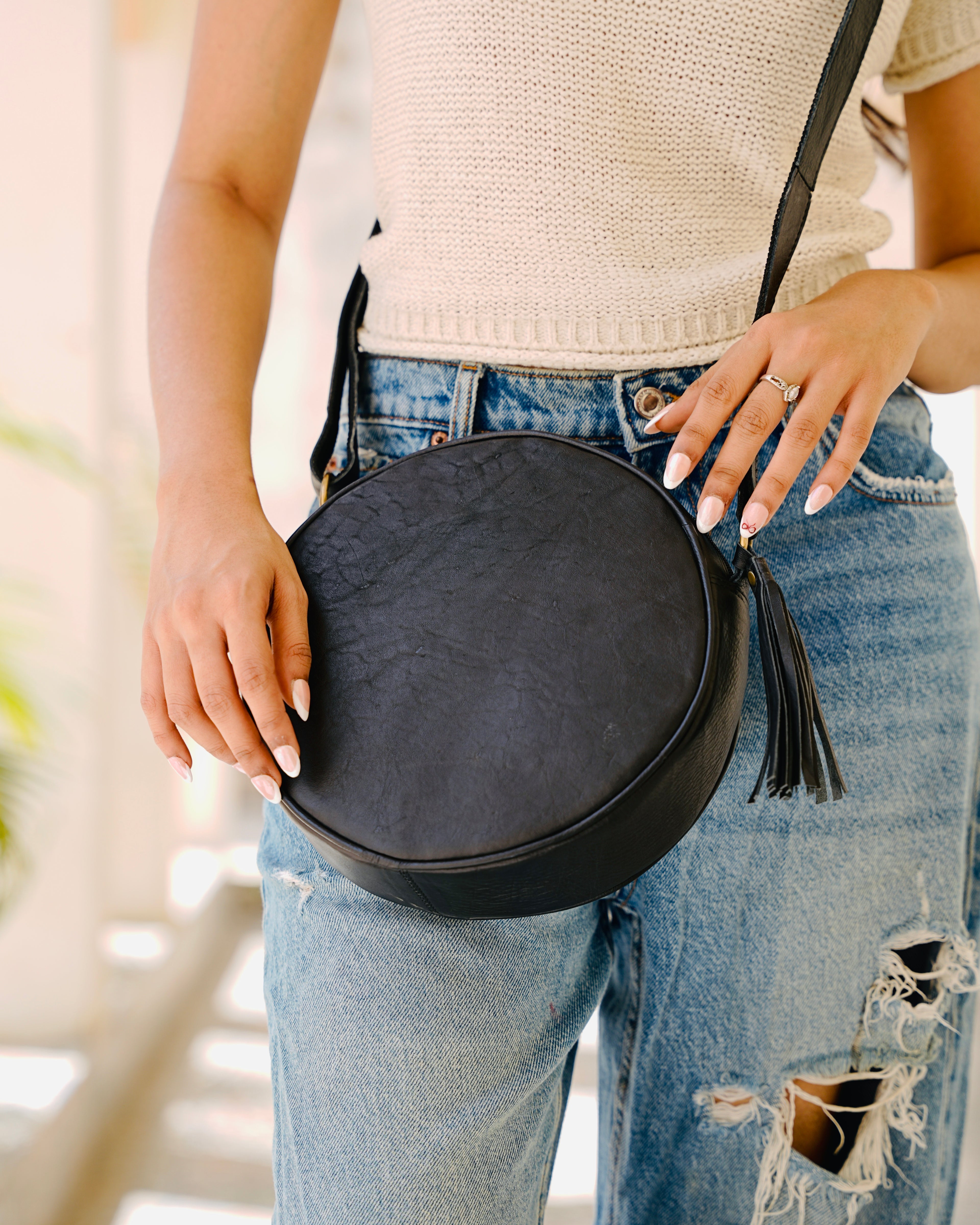 woman holding a black sling crossbody circular aesthetic leather bag