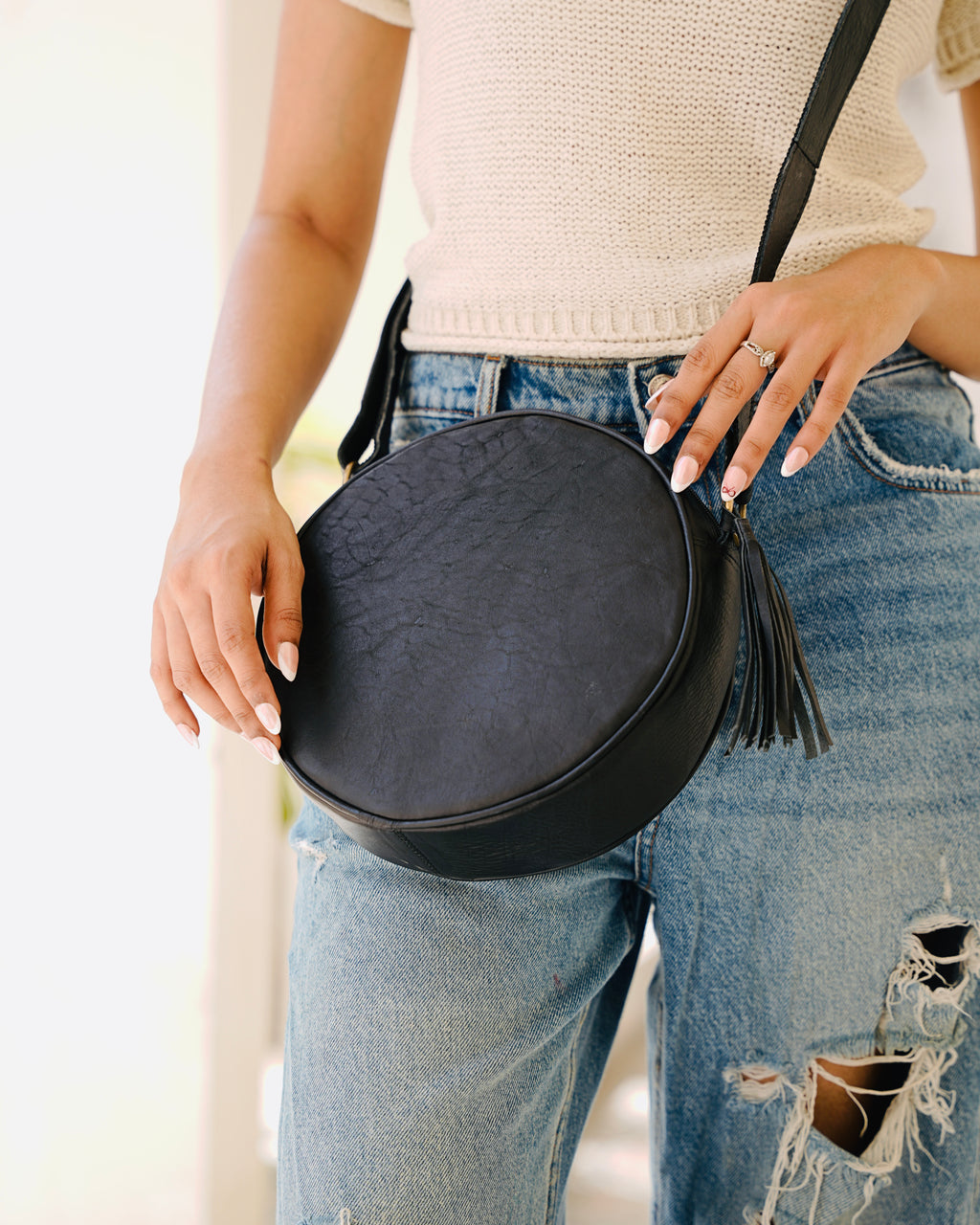 woman holding a black sling crossbody circular aesthetic leather bag
