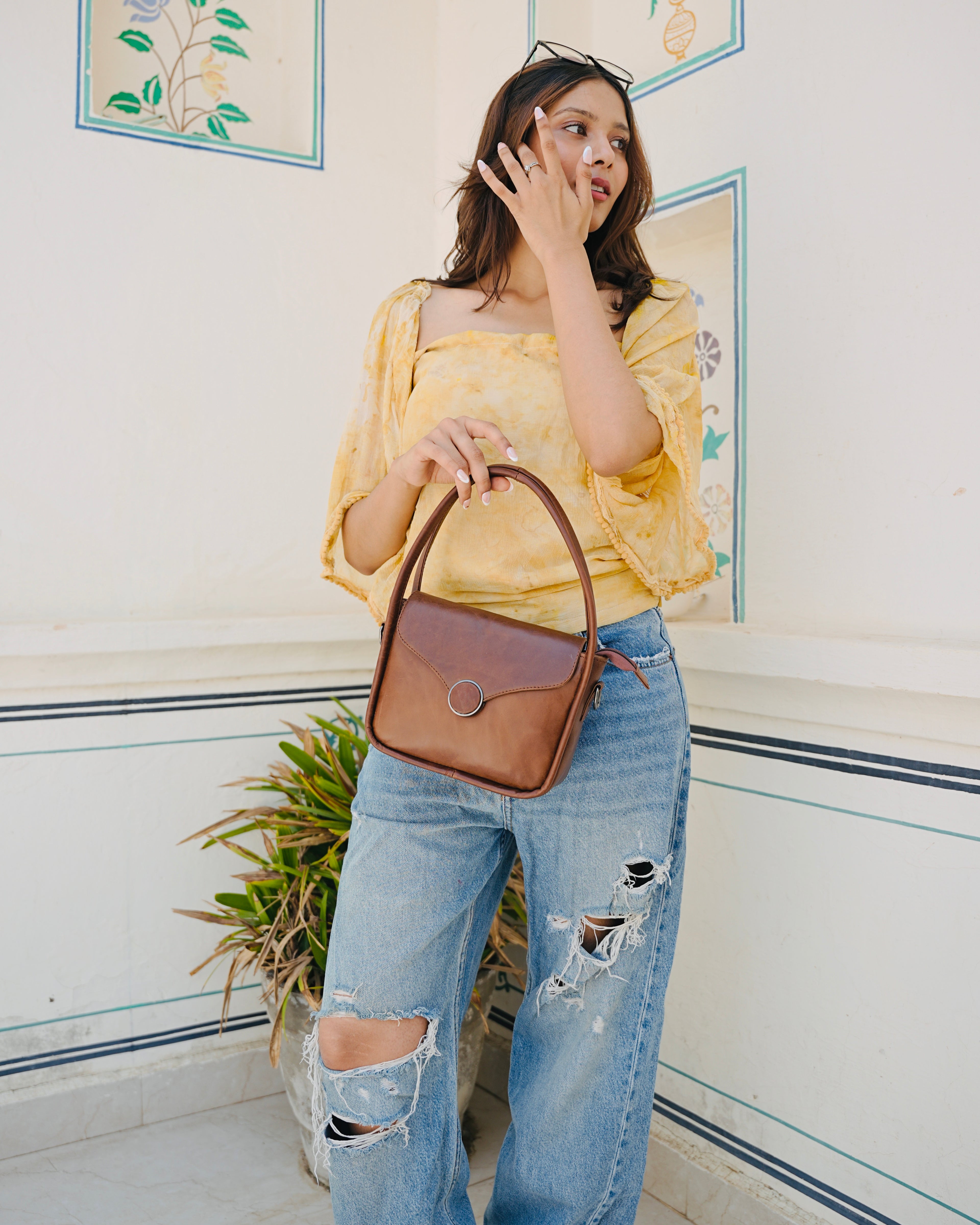Brown buffalo leather handbag held by a person with a aesthetic background
