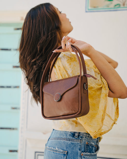 Brown buffalo leather handbag held by a person with a aesthetic background