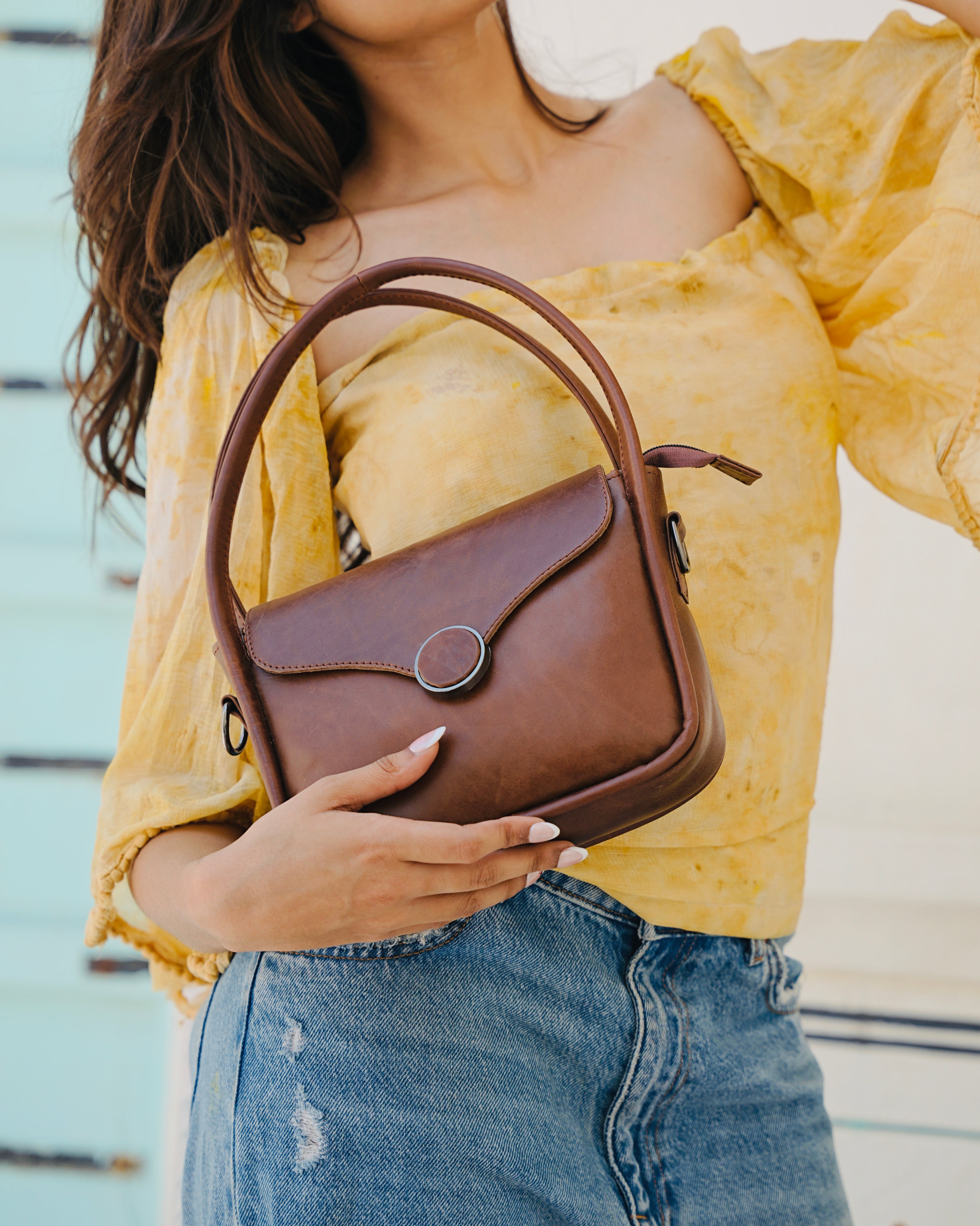 Brown buffalo leather handbag held by a person with a aesthetic background