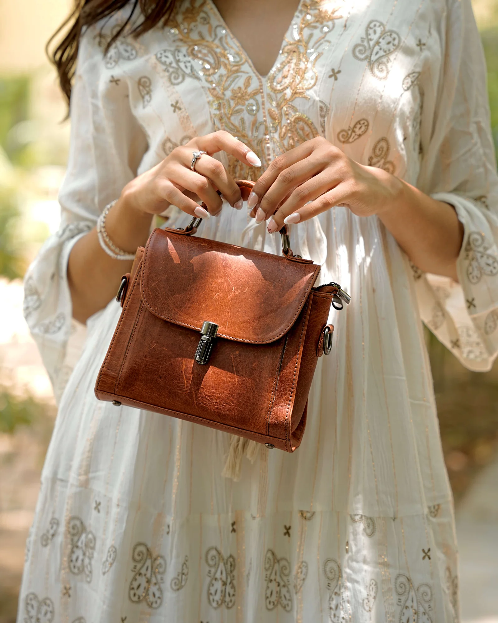 Person holding a genuine brown leather handbag with a blurred natural background. 100% original full grain leather, natural patina